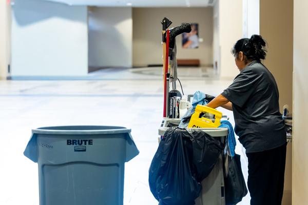 A cleaner with her cart in a building hallway