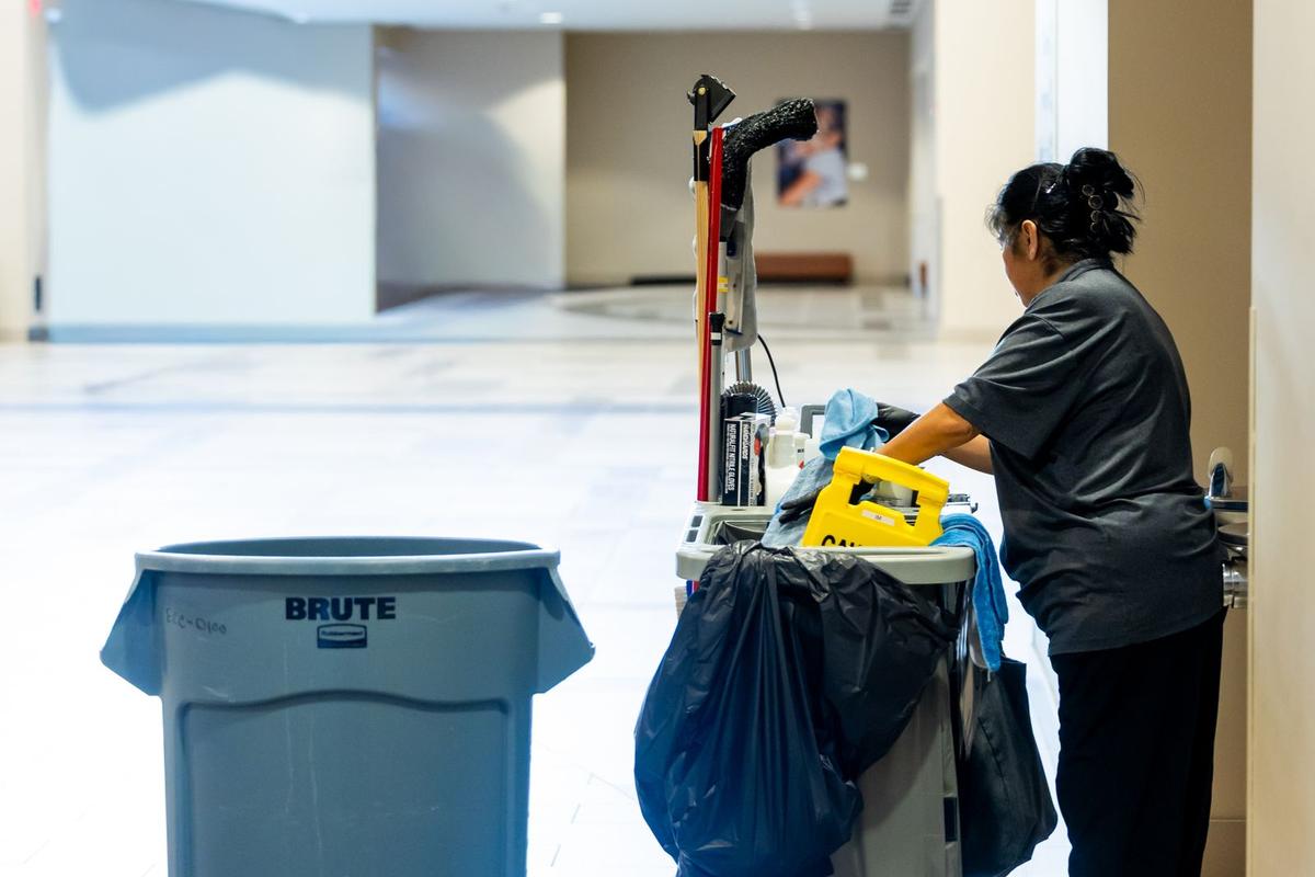 A cleaner with her cart in a building hallway