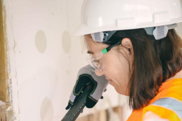 A tradeswoman in a hard hat and safety glasses using a hammer