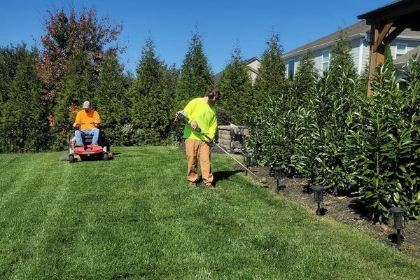 A grounds crew mowing and trimming a large lawn
