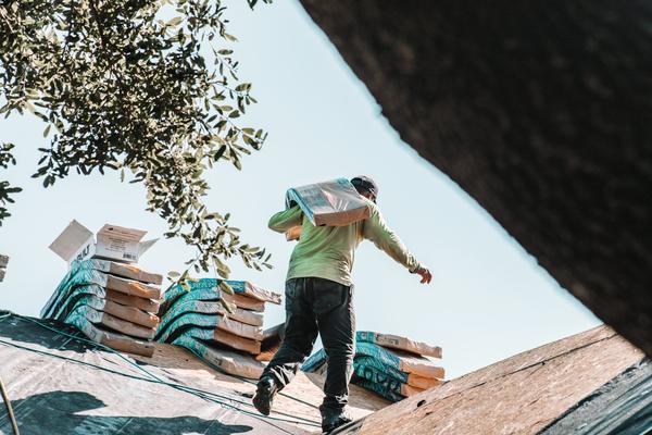 A roofer carrying a bundle of shingles across a roof