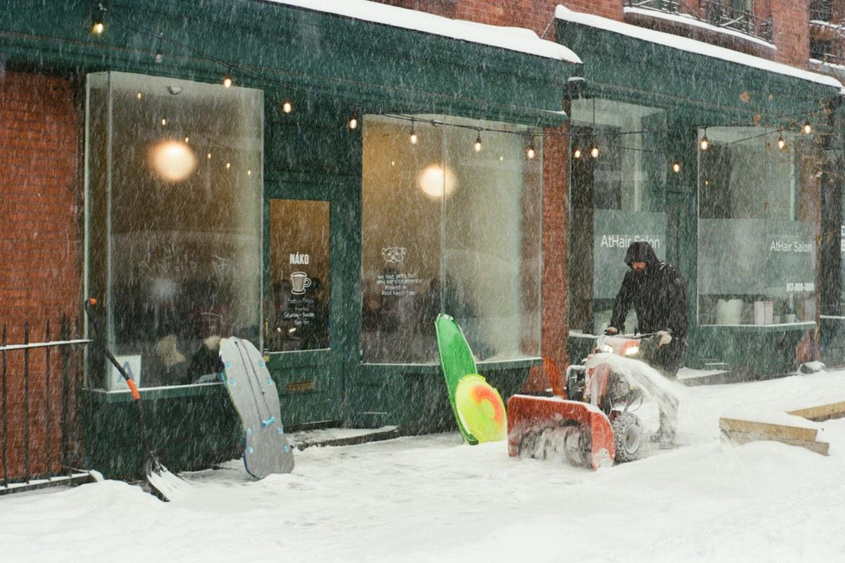 A worker clearing snow outside a shop with a snowblower